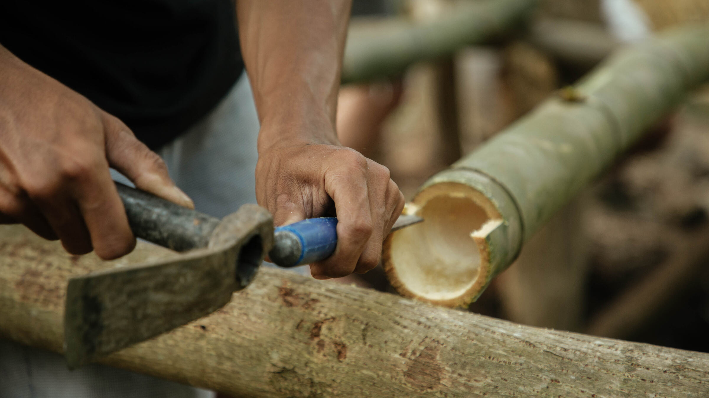 Hands shaping a bamboo pole with a hammer and chisel.