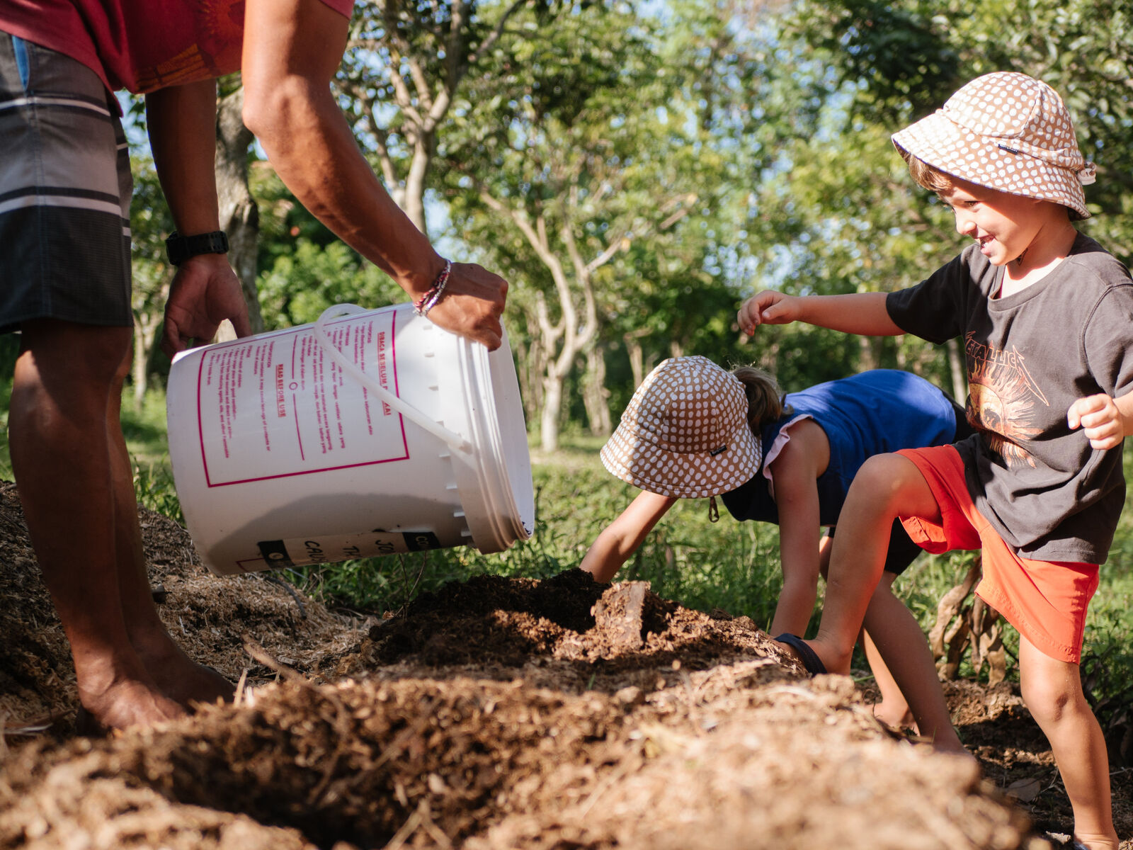 Children pouring compost from a bucket into a garden bed.