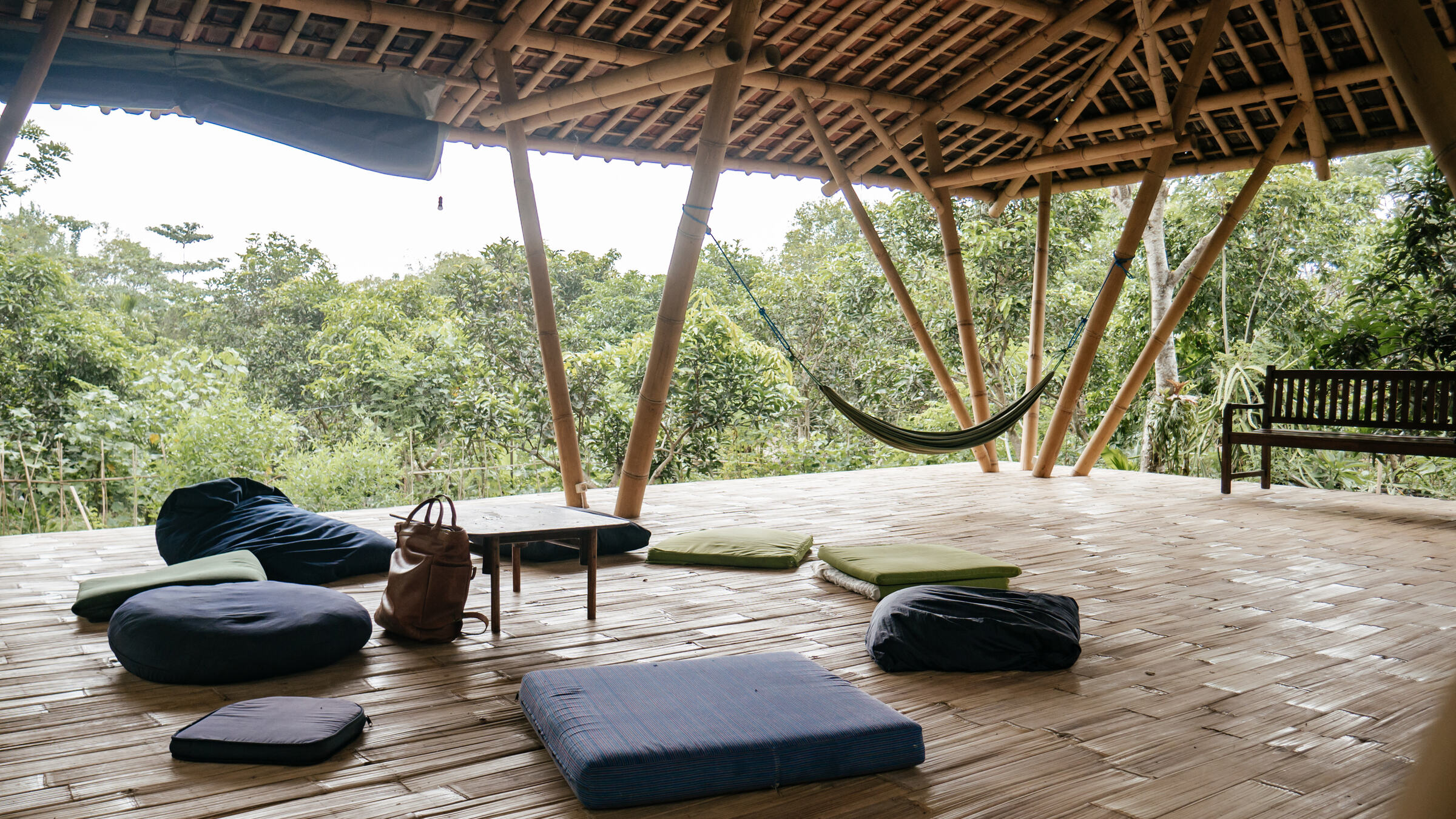 The open bamboo shala with cushions on a woven floor, looking out over the trees.
