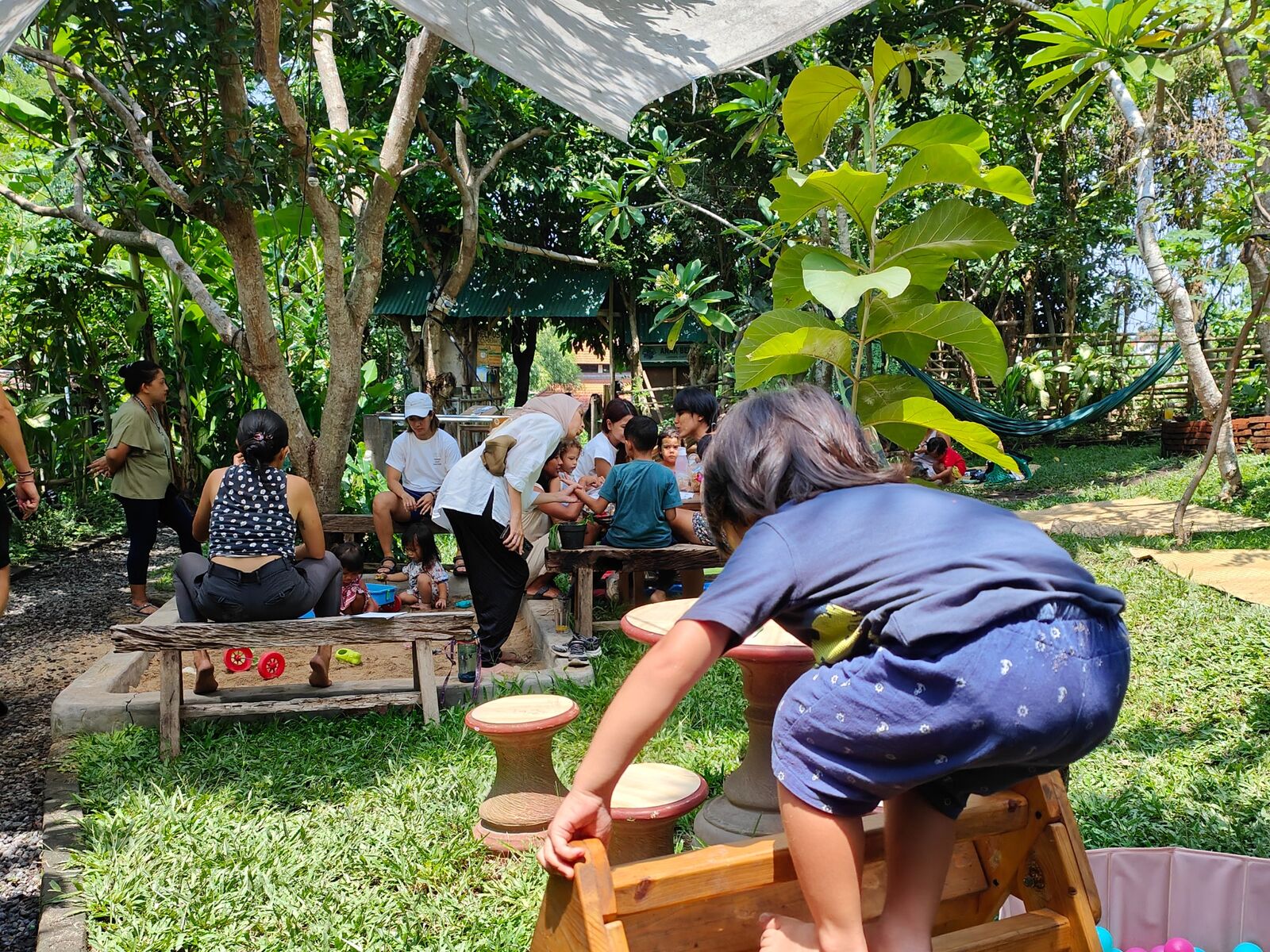 A child climbing on wooden stools in the shaded play area.